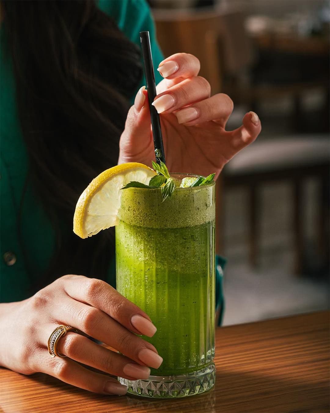 A tall glass of fresh green juice garnished with lemon and mint