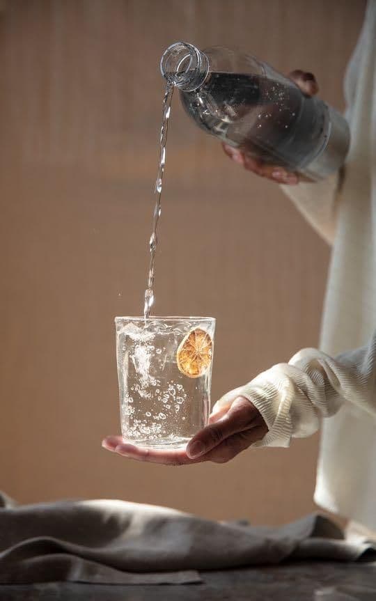 Water being poured from a bottle into a glass held in both hands