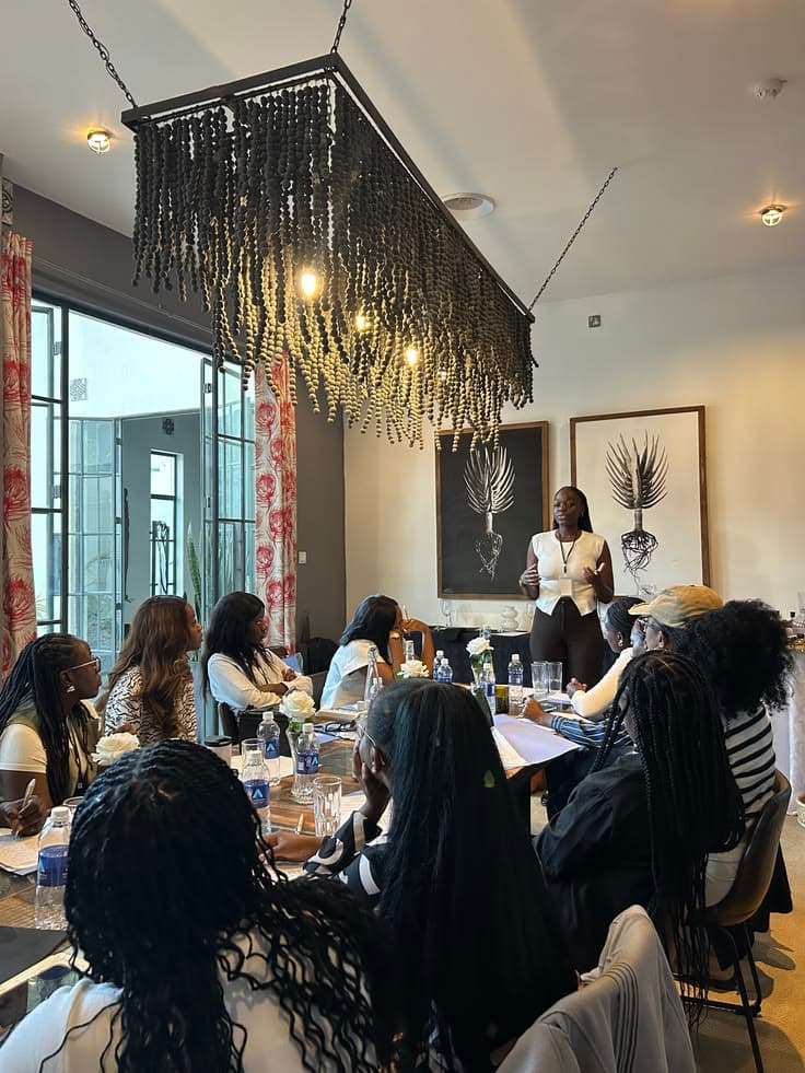 A host addressing guests seated around a long workshop table
