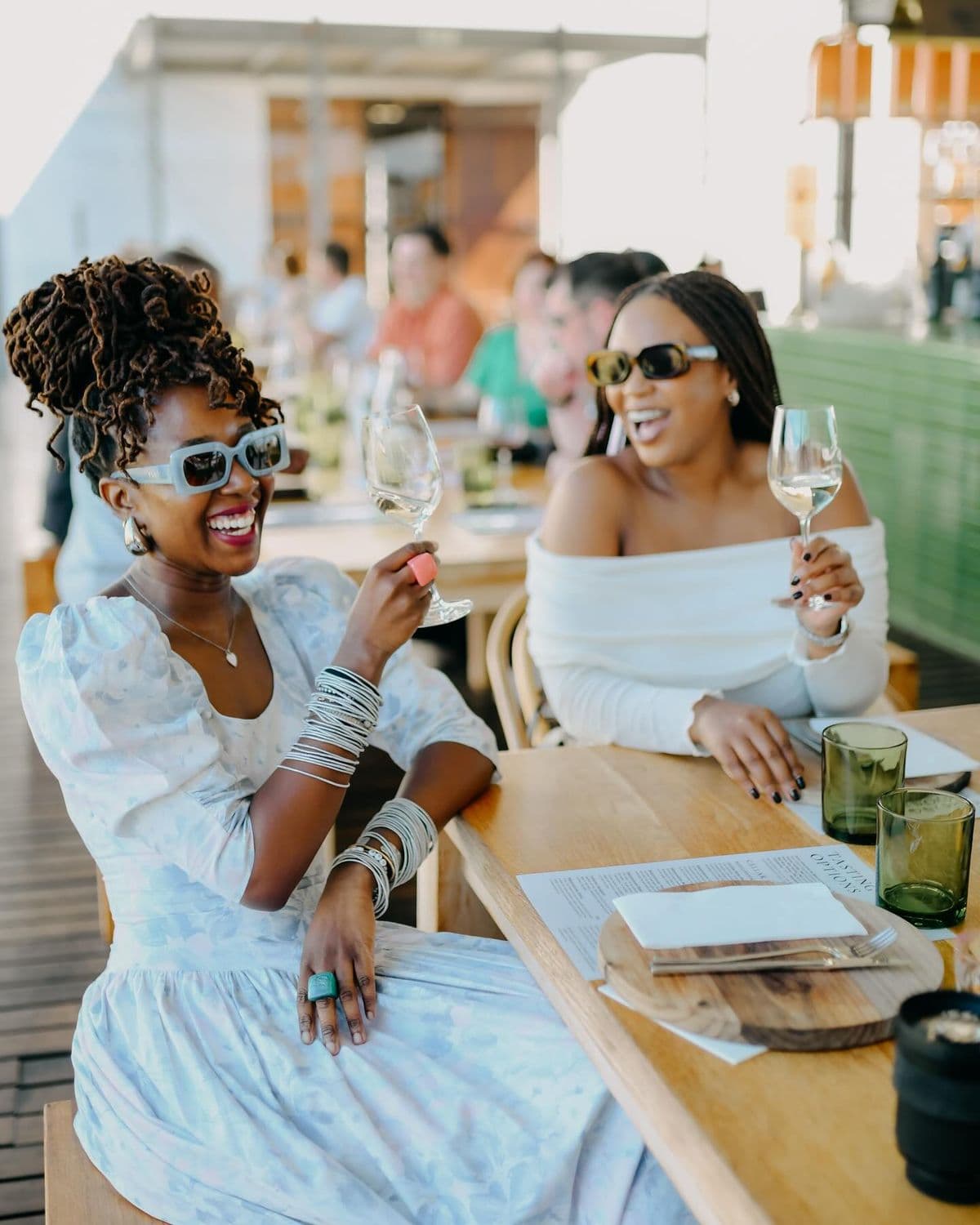 Two friends laughing over drinks at an open-air restaurant